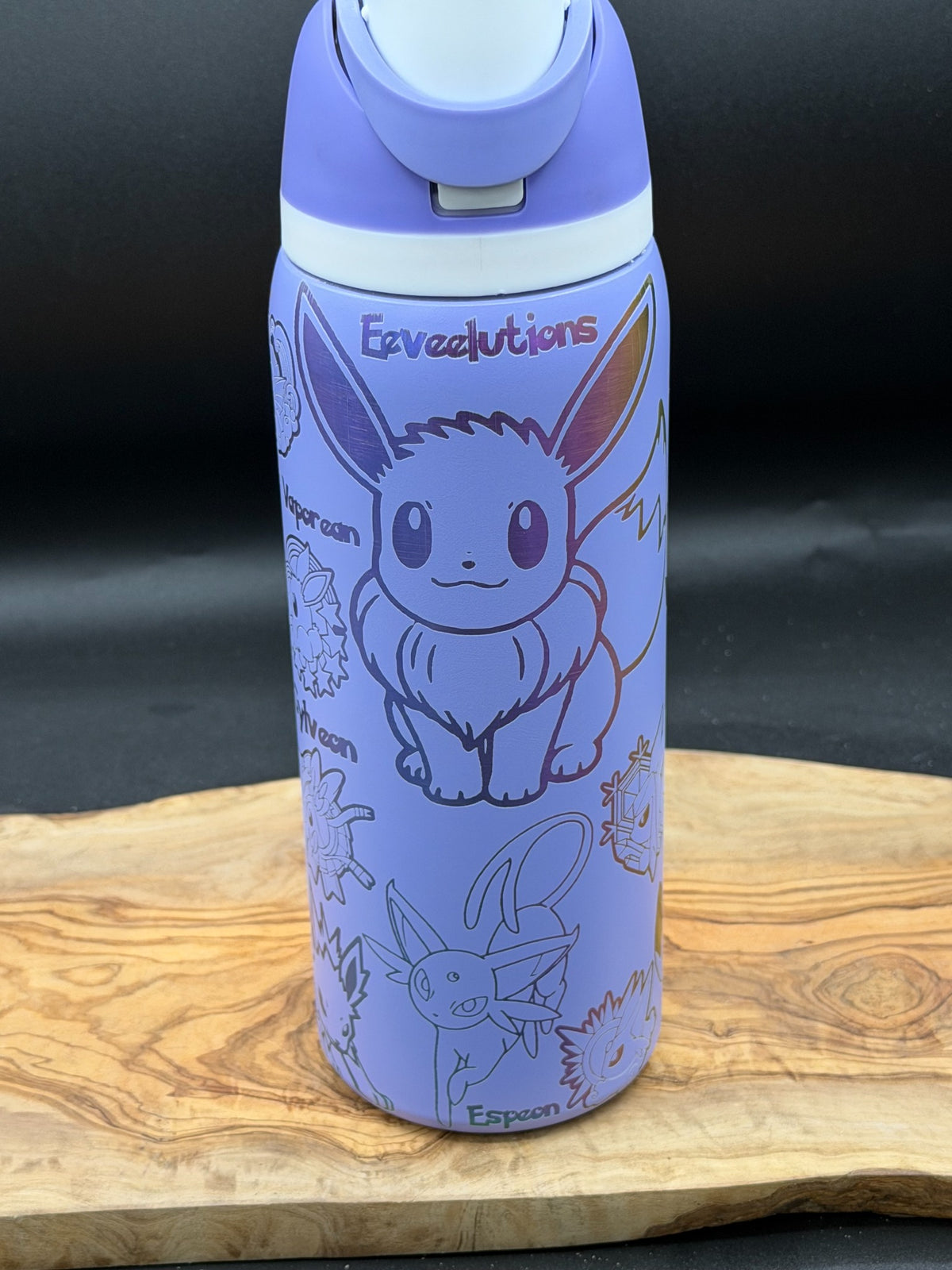 A light purple insulated water bottle with Eevee line art and the word 'Eveevutions' printed on it, shown standing on a wooden surface against a dark background.