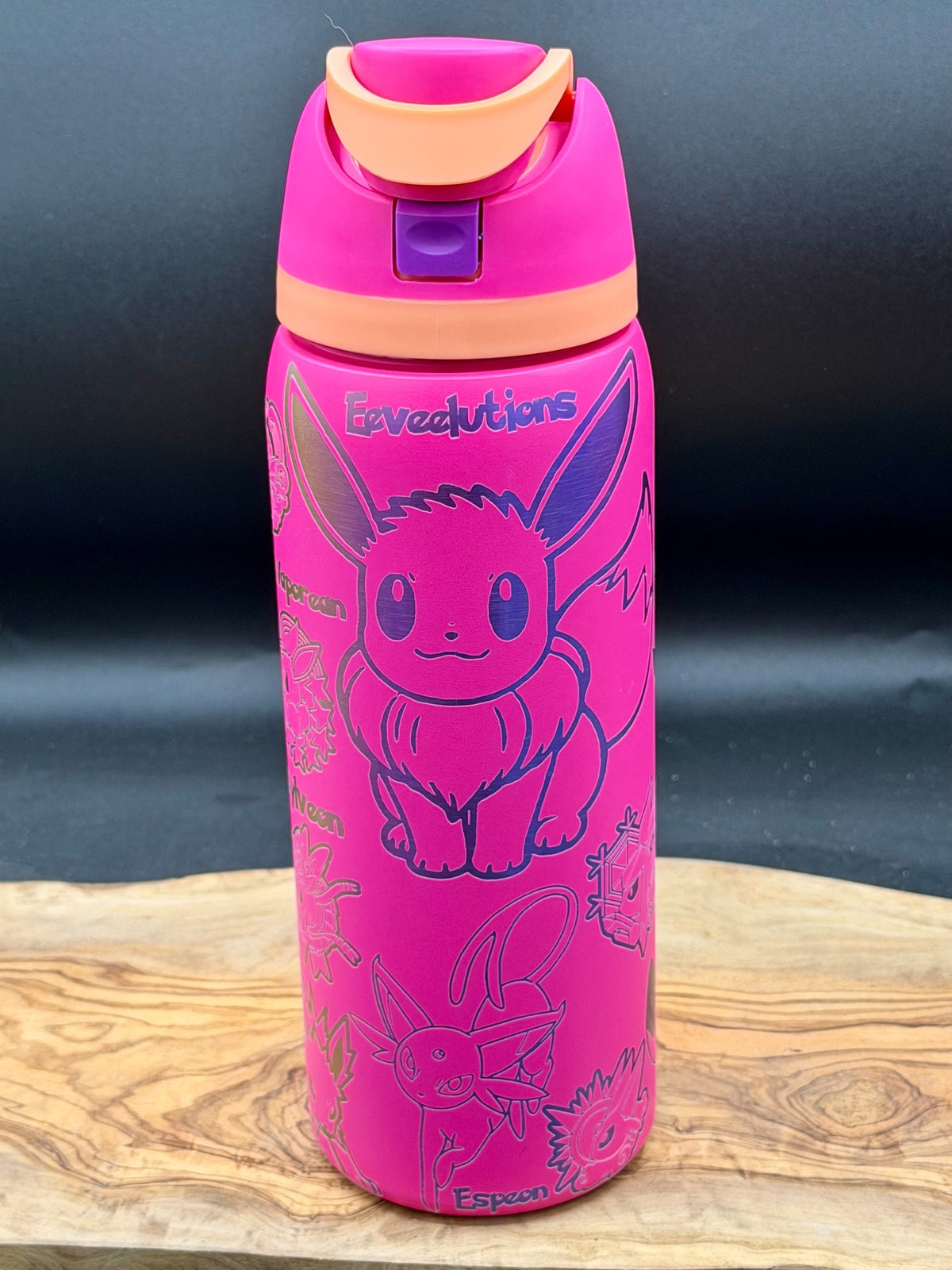 A bright pink insulated water bottle featuring Eevee illustrations and the text 'Evacuations' and 'Eevee', with a matching pink lid and orange flip spout, displayed on a wooden surface against a dark background.