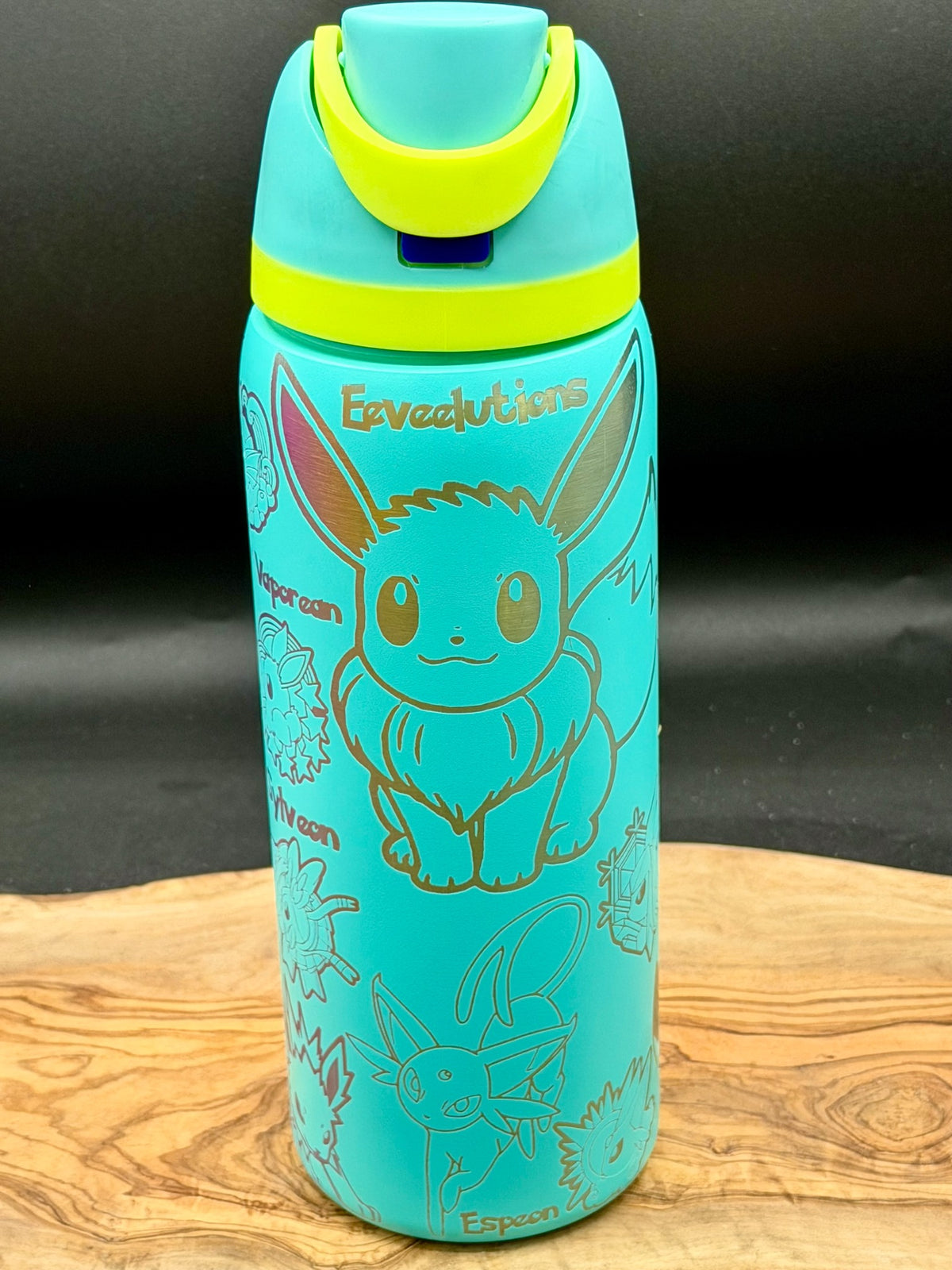 A turquoise water bottle featuring a gold-colored outline of the Pokémon Eevee, with the word 'Eveevutions' printed near the top. The bottle has a matching turquoise lid with a bright yellow-green flip-top spout, and is displayed on a wooden surface against a dark background.